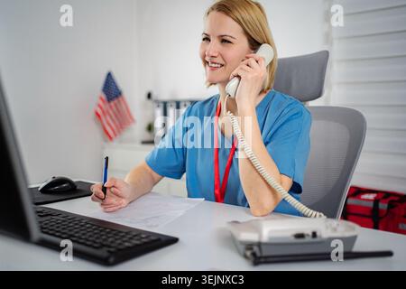 Female nurse talking on phone and making notes in medical office Stock Photo