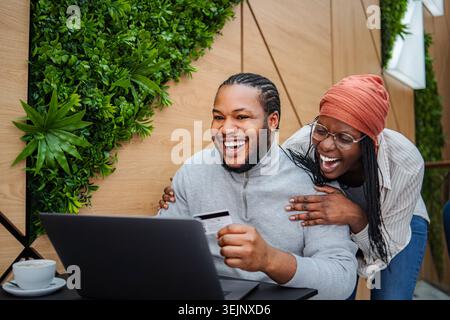 Young adult couple smiling while holding a credit card and using a laptop for online shopping Stock Photo