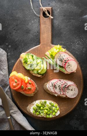 Different vegan sandwiches with vegetables, radish, tomato, rye bread on black. Appetizer for party. Stock Photo