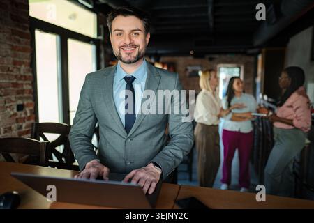Confident businessman standing with laptop while colleagues talk Stock Photo