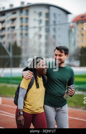 Diverse couple smiling, embracing on running track, enjoying fitness Stock Photo