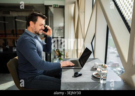 Man working on laptop and talking on mobile phone Stock Photo