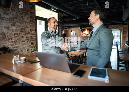 Businessmen shaking hands making partnership deal in cafe Stock Photo