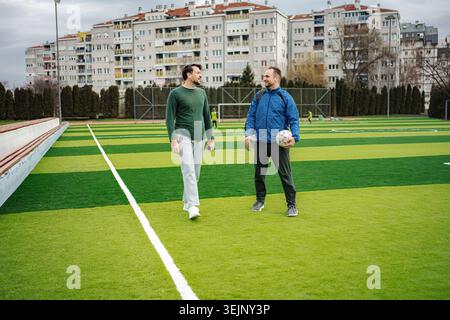 Male friends walking on soccer field talking Stock Photo