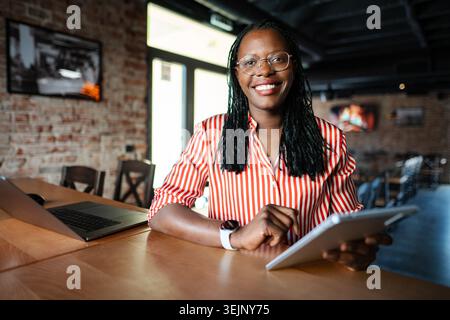 African American businesswoman smiling using tablet in cafe Stock Photo