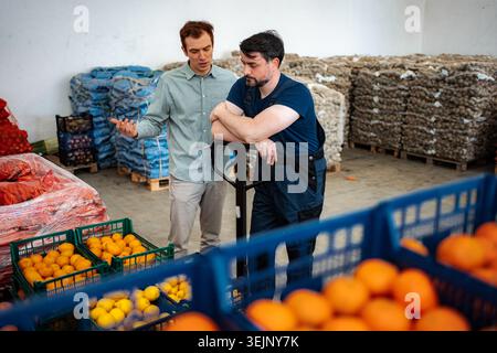 Employee and manager discussing logistics in produce warehouse Stock Photo