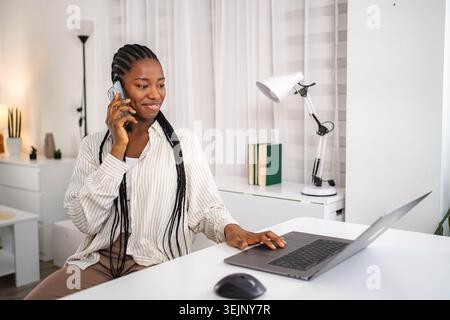 Young woman telecommuting, talking on smartphone and using laptop Stock Photo