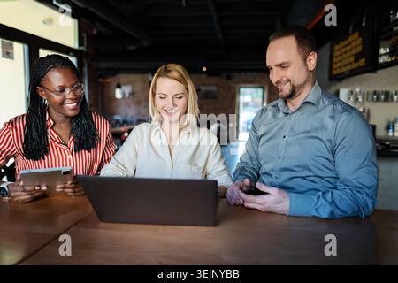 Three diverse colleagues collaborating on laptop in modern cafe Stock Photo