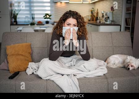 Woman blowing nose with tissue having cold symptoms at home Stock Photo