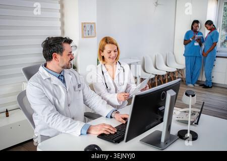 Doctors and nurses collaborating in clinic using computer and document Stock Photo