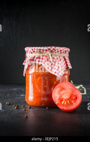 Homemade adjika with tomatoes in jar on dark background. Stock Photo
