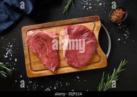 Raw marbled ribeye steak with rosemary sprig on black background. Stock Photo