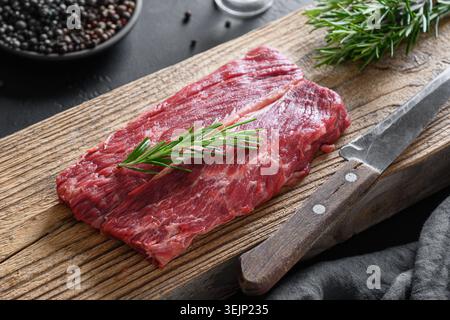 Raw marbled ribeye steak with rosemary sprig on woden cutting board. Close up. Stock Photo