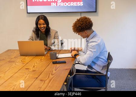 Diverse coworkers in business attire typing on laptop and writing printed document in meeting room. Collaboration, professionali Stock Photo