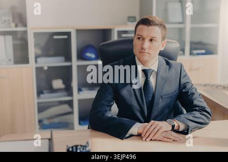 Portrait of thoughtful businessman in elegant suit sits in office at his cabinet, ponders on creating new business plan, ponders Stock Photo