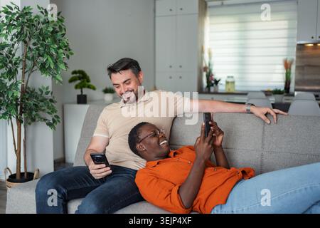 Interracial couple relaxing on sofa using smartphones at home Stock Photo