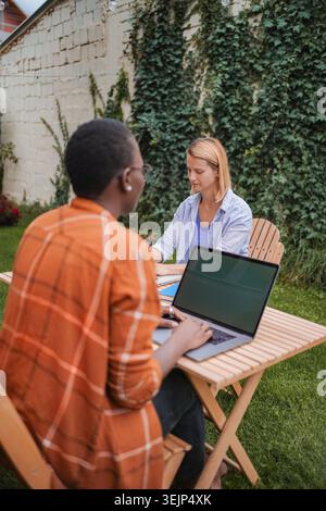 Two young women working outdoors on a laptop in the garden Stock Photo