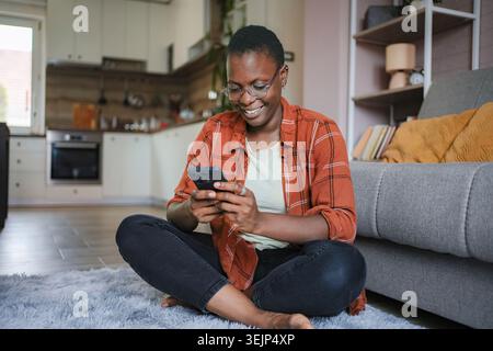 Smiling young woman using mobile phone at home Stock Photo