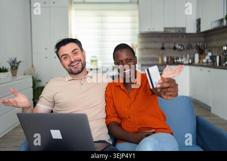 Young multiethnic couple is buying online using laptop and credit card at home Stock Photo