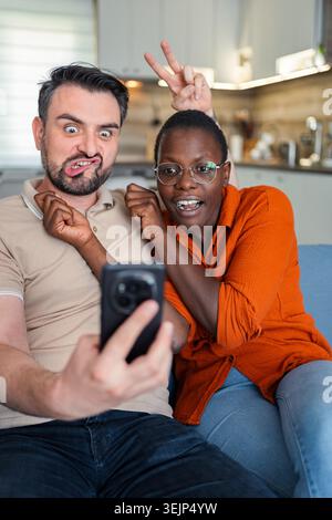 Playful couple making funny faces while taking a selfie at home Stock Photo