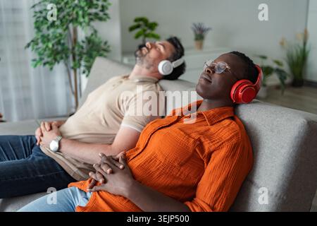 Serene couple relaxing on sofa, enjoying music with headphones Stock Photo