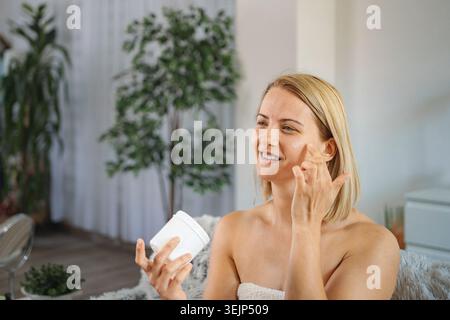 Young woman applying face cream at home Stock Photo