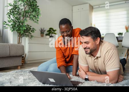Happy couple smiling and using laptop at home Stock Photo