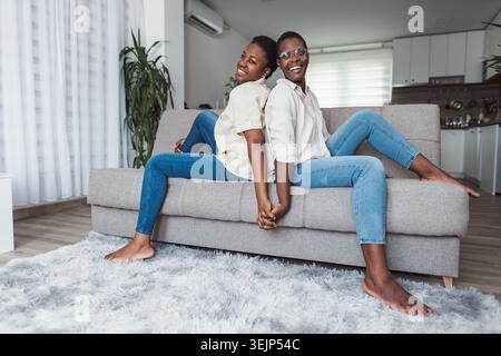 Two Young Women Holding Hands and Relaxing on Sofa at Home Stock Photo