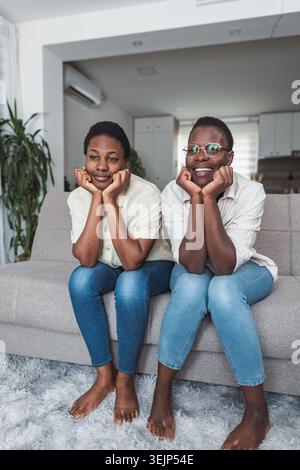 Two african women sitting on couch watching television at home Stock Photo