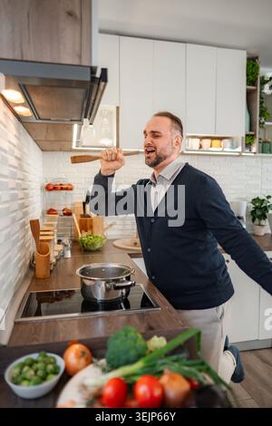 Man singing in kitchen using wooden spoon as microphone Stock Photo