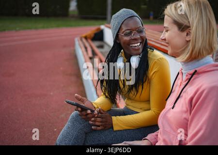 Diverse women friends talking using smartphone on running track Stock Photo