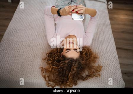 Young woman lying on bed using smartphone for selfie Stock Photo