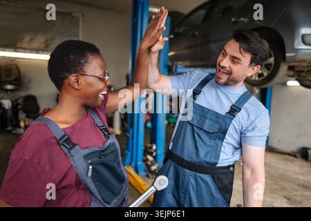 Two happy mechanics giving high five after repairing car in auto repair shop Stock Photo