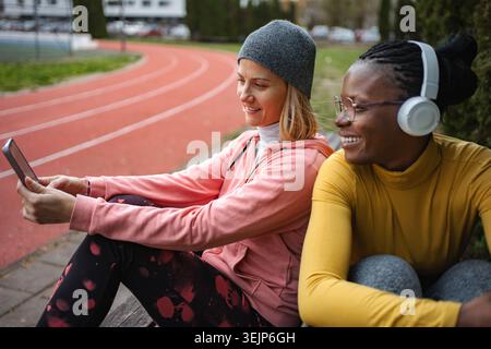 Two smiling women friends relaxing at running track using smartphone Stock Photo