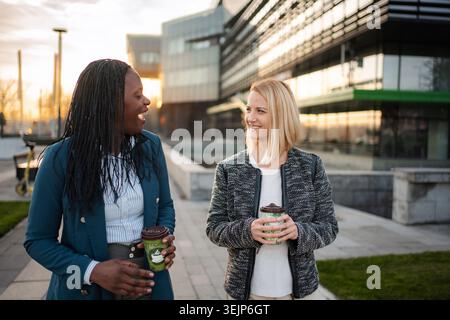 Diverse businesswomen walking, talking, drinking coffee on urban break Stock Photo
