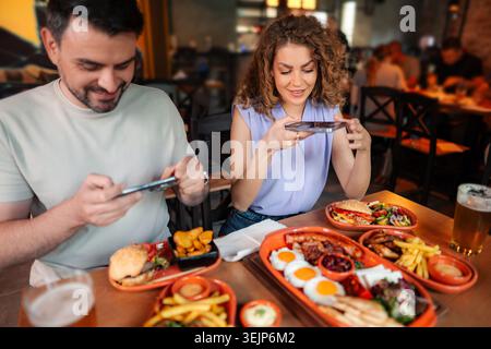 Young couple taking pictures of their food in a restaurant using their smartphones Stock Photo