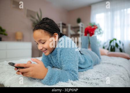 Enjoying a cozy afternoon playing games on a smartphone while lying on a soft blanket Stock Photo
