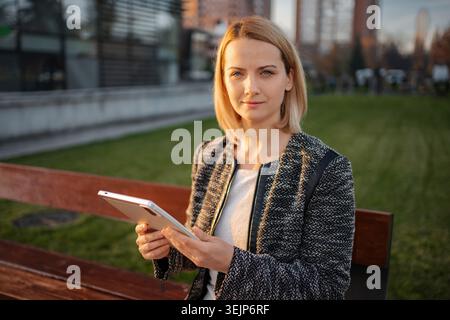 Businesswoman using tablet sitting on bench in city park Stock Photo