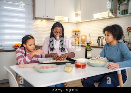 Mother and daughters preparing pizza together in kitchen Stock Photo