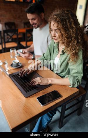 Young woman working on laptop in cafe while man using smartphone Stock Photo
