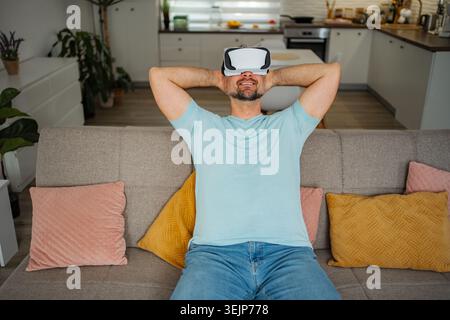 Man wearing a VR headset on a couch, smiling and relaxing Stock Photo