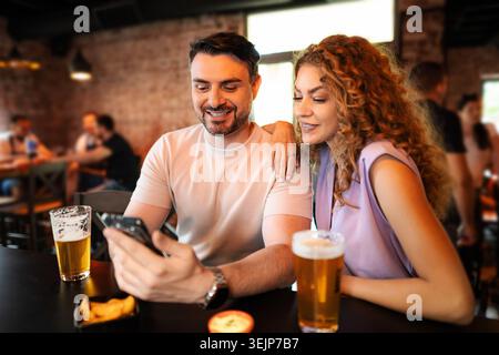 Couple enjoying beer and using smartphone in pub Stock Photo