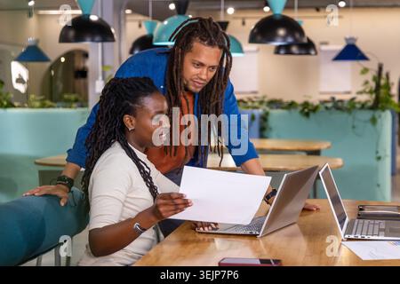 African American team collaborating, reviewing printed sheet and laptops in casual wear at table. Coworking, collaboration, prod Stock Photo