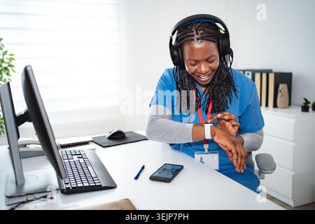 Healthcare worker wearing headphones using smartwatch at desk Stock Photo