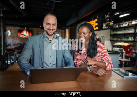 Diverse business professionals collaborating on laptop in cafe Stock Photo