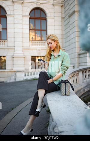 Woman sitting on street in Vienna using smartphone Stock Photo