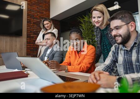 A diverse group of individuals are seated together, focused on a laptop computer in front of them. They appear engaged in discussions, collaboration, Stock Photo