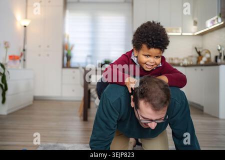 Father giving piggyback ride to happy son at home Stock Photo