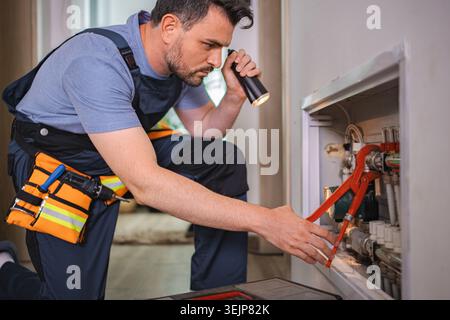 Plumber working on pipes, using flashlight and wrench Stock Photo