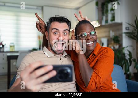 Playful couple taking a selfie making funny faces at home Stock Photo